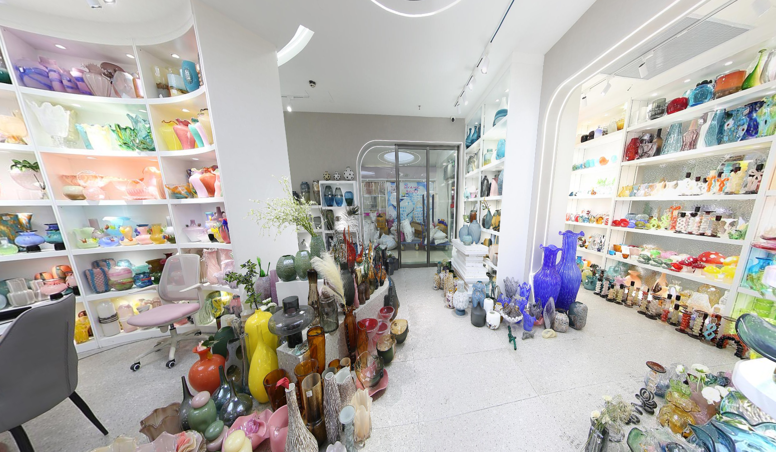 Walkway inside a Yiwu glass decor showroom with an arched entrance, pastel display shelves on the left, and colorful glass vases and decorative items on the right.