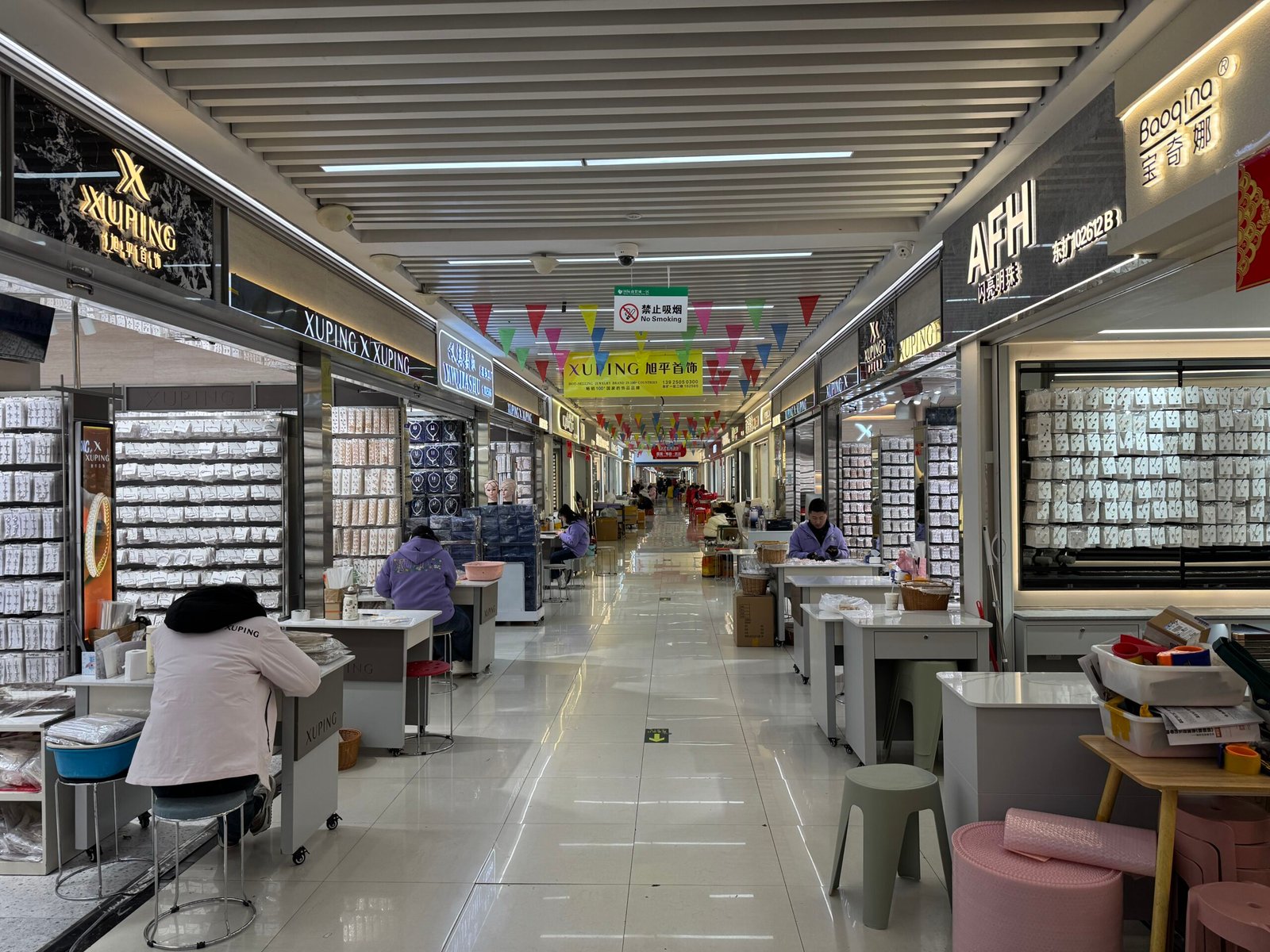 Indoor corridor of the Yiwu jewelry wholesale market with accessory stalls, XUPING shop signs, and vendors at counters.