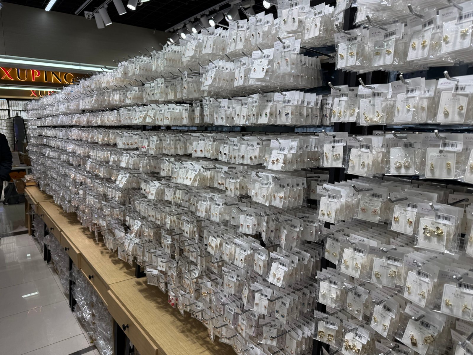 Rows of XUPING earrings in sealed retail packaging hanging on display racks at a Yiwu jewelry wholesale stall.