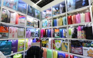 Sample display of custom non-woven shopping bags in Yiwu Market showing various sizes, colors, printed logos, laminated finishes, and handle styles from a bag manufacturer