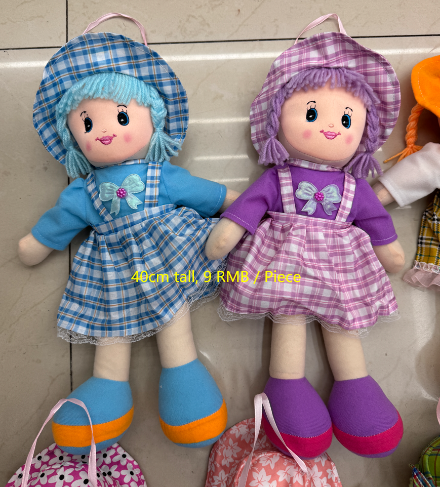 Two colorful wholesale soft cloth rag dolls with plaid hats, blue and purple dresses, embroidered faces, and yarn hair at Yiwu Toy Market
