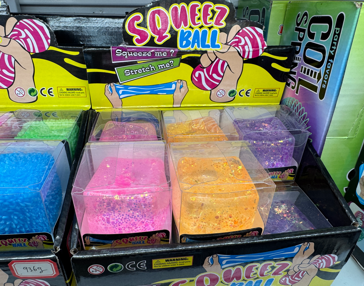 Wholesale glitter squeeze cube balls with transparent gel texture, sparkling beads, and bright pink, orange, blue, green, and purple colors, displayed in clear boxes at Yiwu Toy Market.
